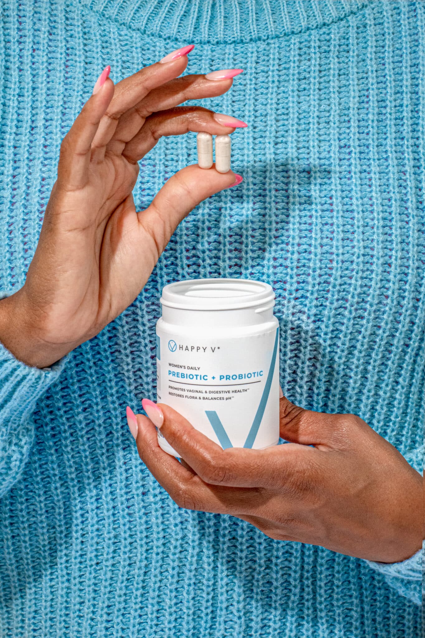 A close-up of someone holding two prebiotic and probiotic supplements from Happy V.