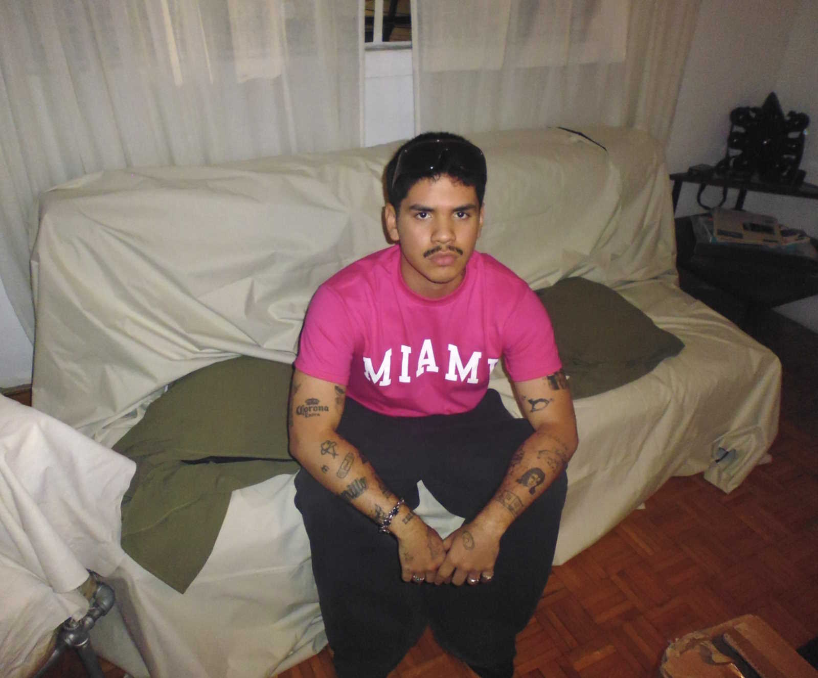 Promotional image of Andry Kiddos. He is sitting. He is wearing a pink shirt with the word MIAMI.
