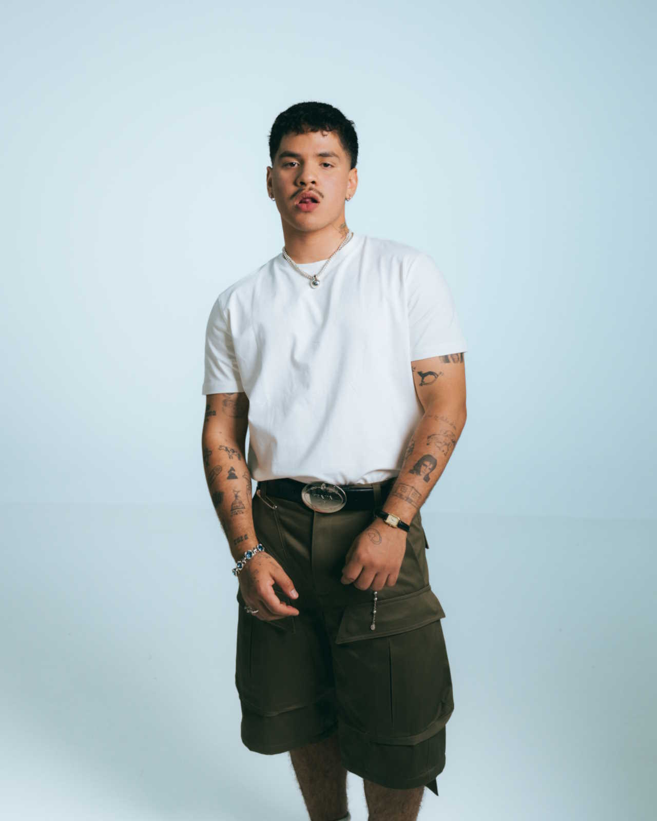 Promotional image of Andry Kiddos. He is standing in front of a white background. He is wearing a short-sleeve white t-shirt and olive green cargo shorts.